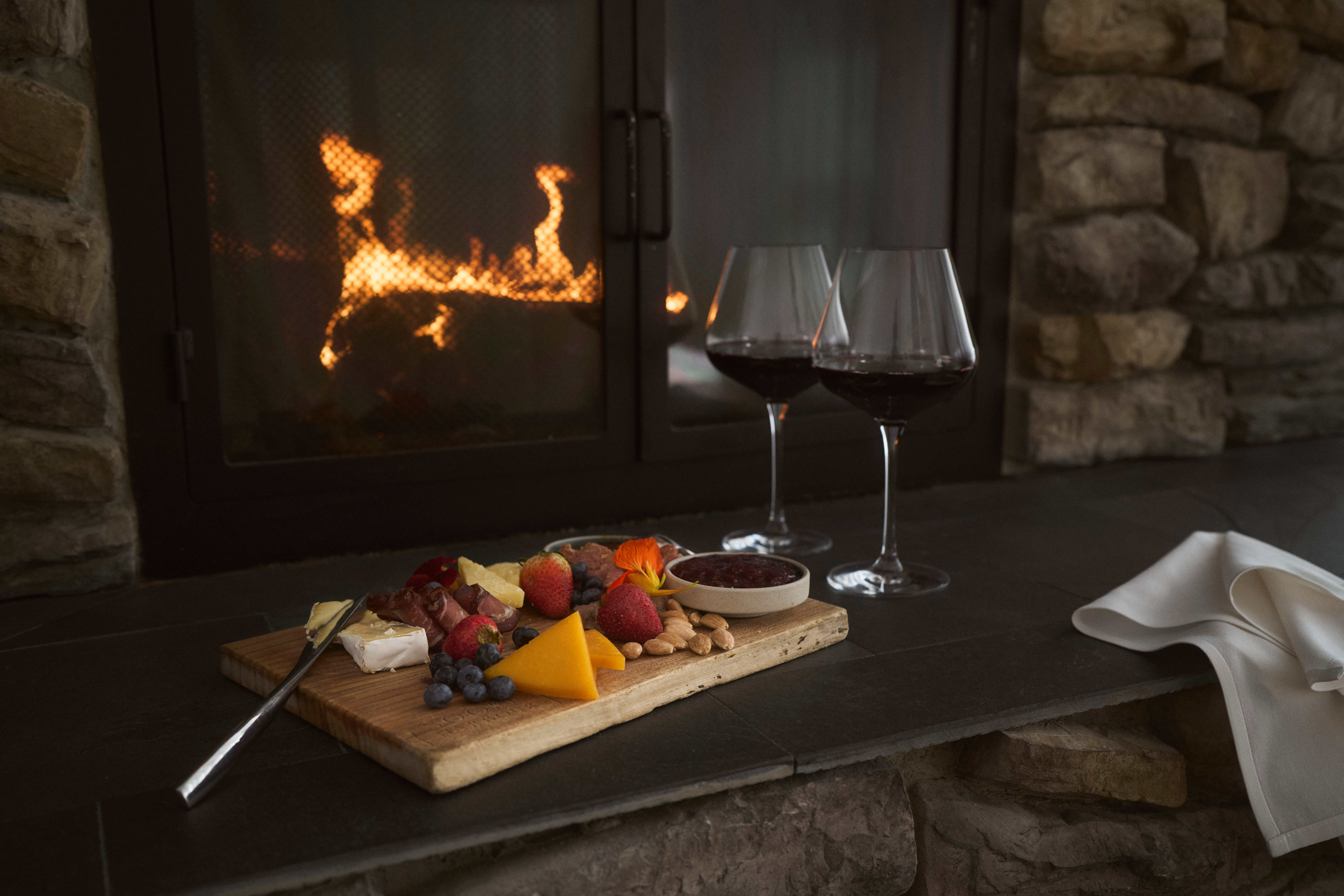 Two glasses of wine and a charcuterie spread in front of a cozy fireplace at Sooke Harbour House