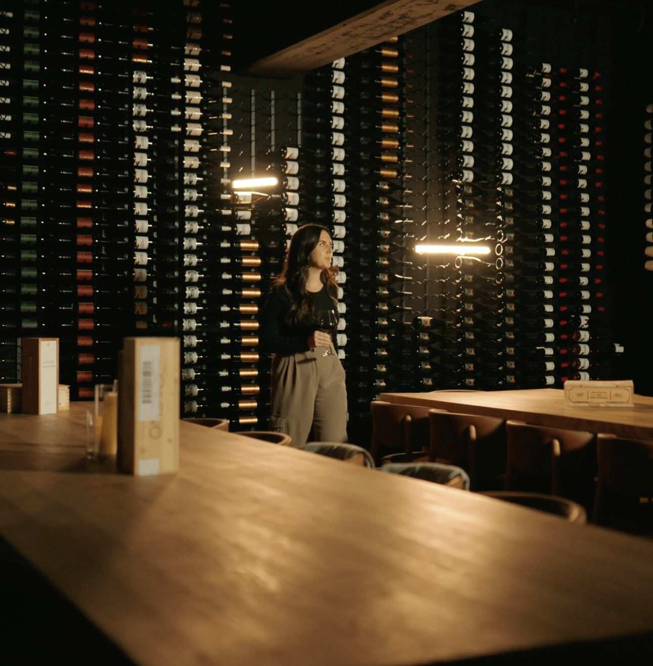 A woman holds a glass of wine in the Wine Cellar, a room filled with walls of unique bottles of wine at the Sooke Harbour House